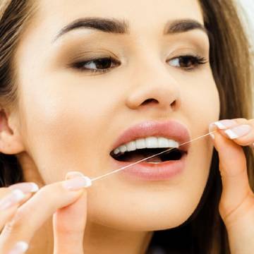 Woman using dental floss for cleaning her teeth | Alvarez Dental